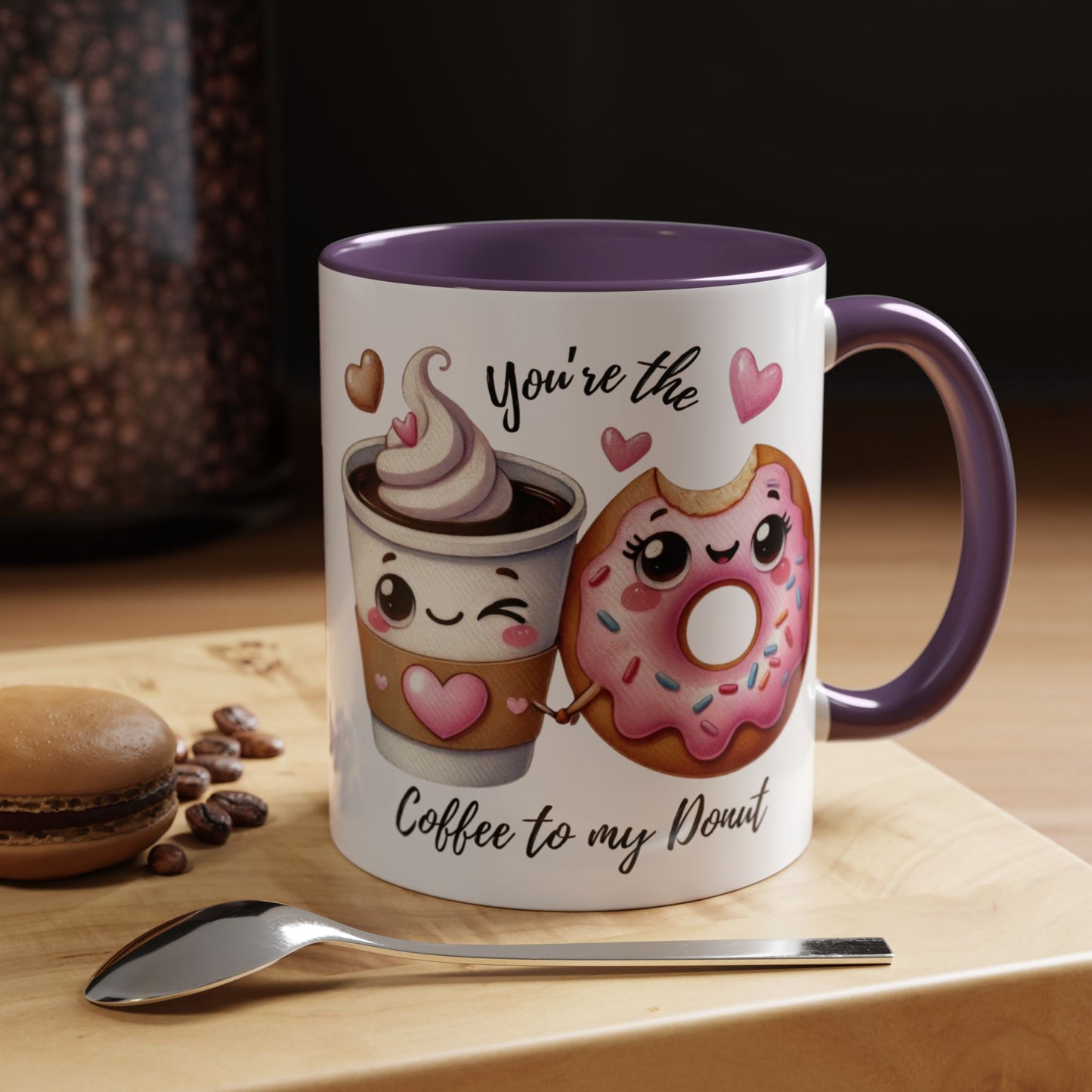 Mug with cartoon coffee cup and donut design, text 'You're the coffee to my donut', on a wooden surface with coffee beans and a spoon.