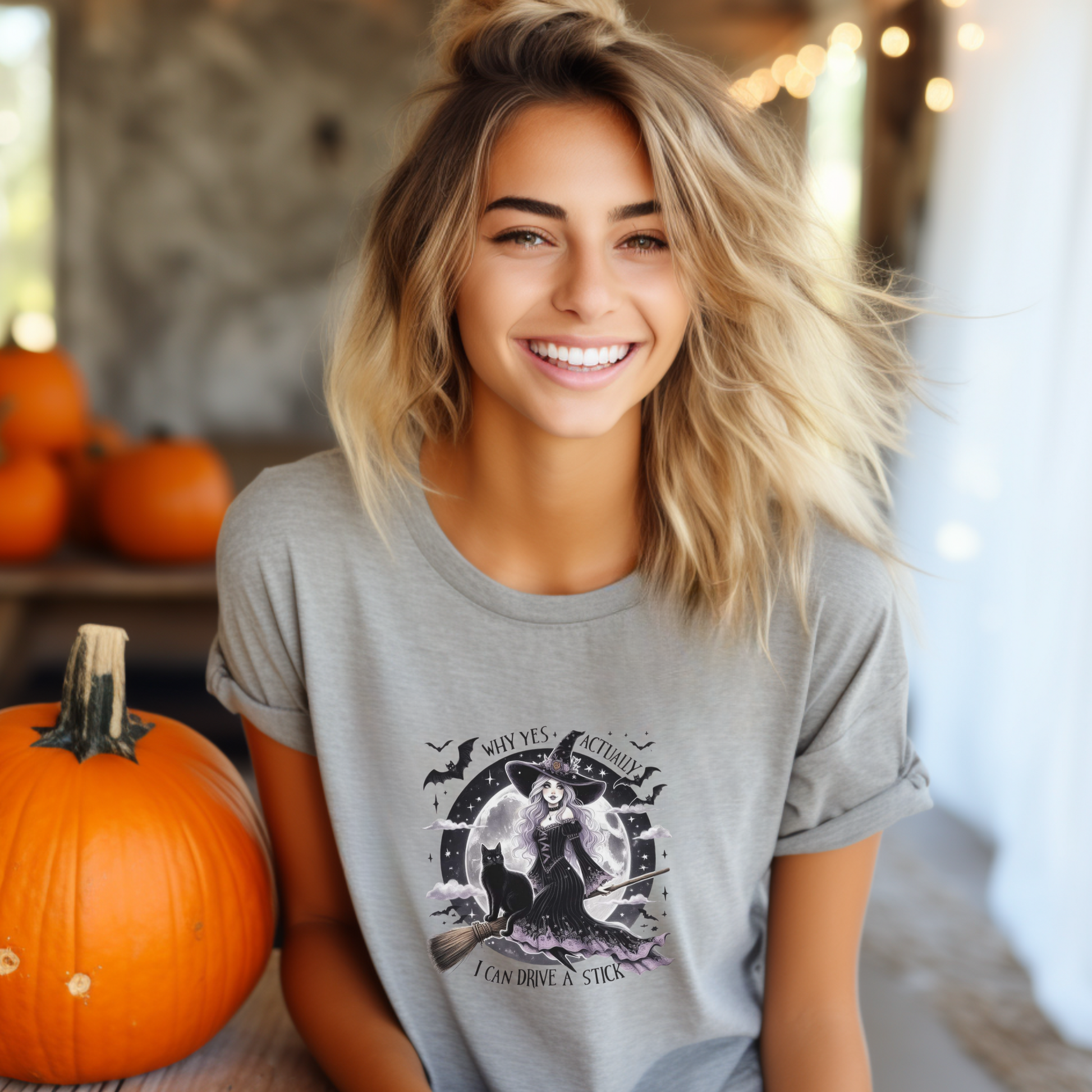 Woman wearing a light grey Halloween-themed t-shirt with pumpkins in the background,  why yes actually, i can drive a stick, 
