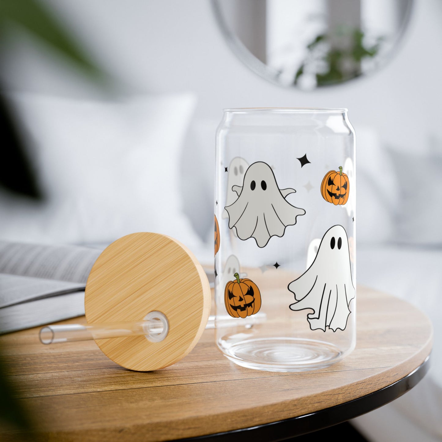 Clear glass tumbler with Halloween-themed design of ghosts and pumpkins on a wooden table.