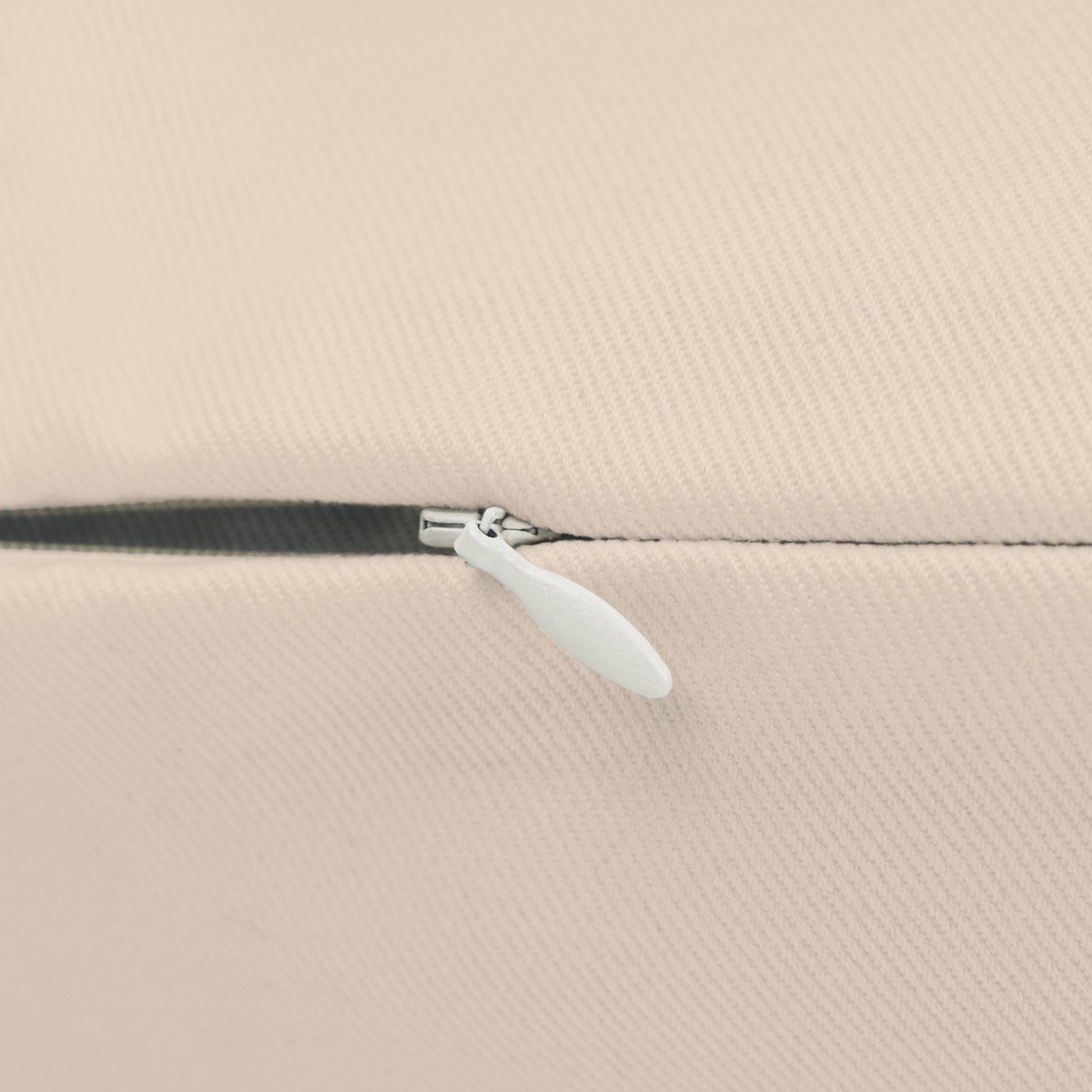 Close-up of a beige fabric with a zipper and white pull tab.
