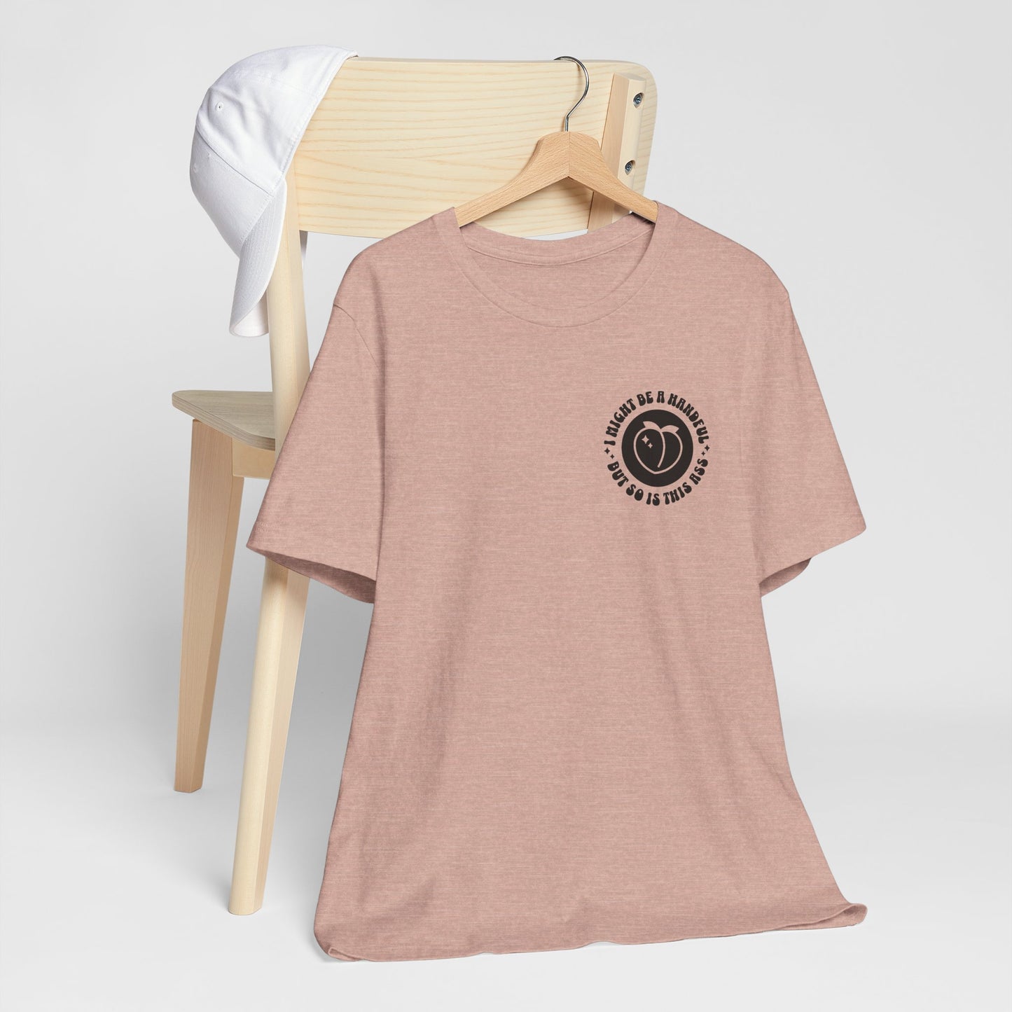 heather peach t-shirt with a black graphic on a wooden hanger against a white background, i might be a handful but so is this ass