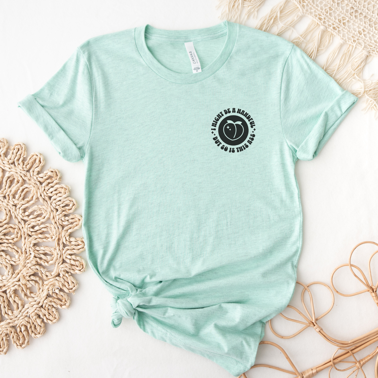 Mint green t-shirt with a black graphic design on a white surface with decorative elements.  I might be a handful but so is this ass