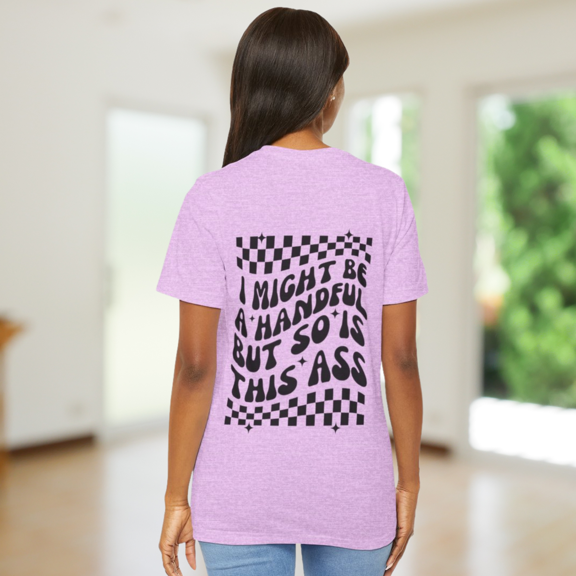 Person wearing a light purple t-shirt with text and checkered pattern on the back, standing in a room with a blurred background. i might be a handful but so is this ass