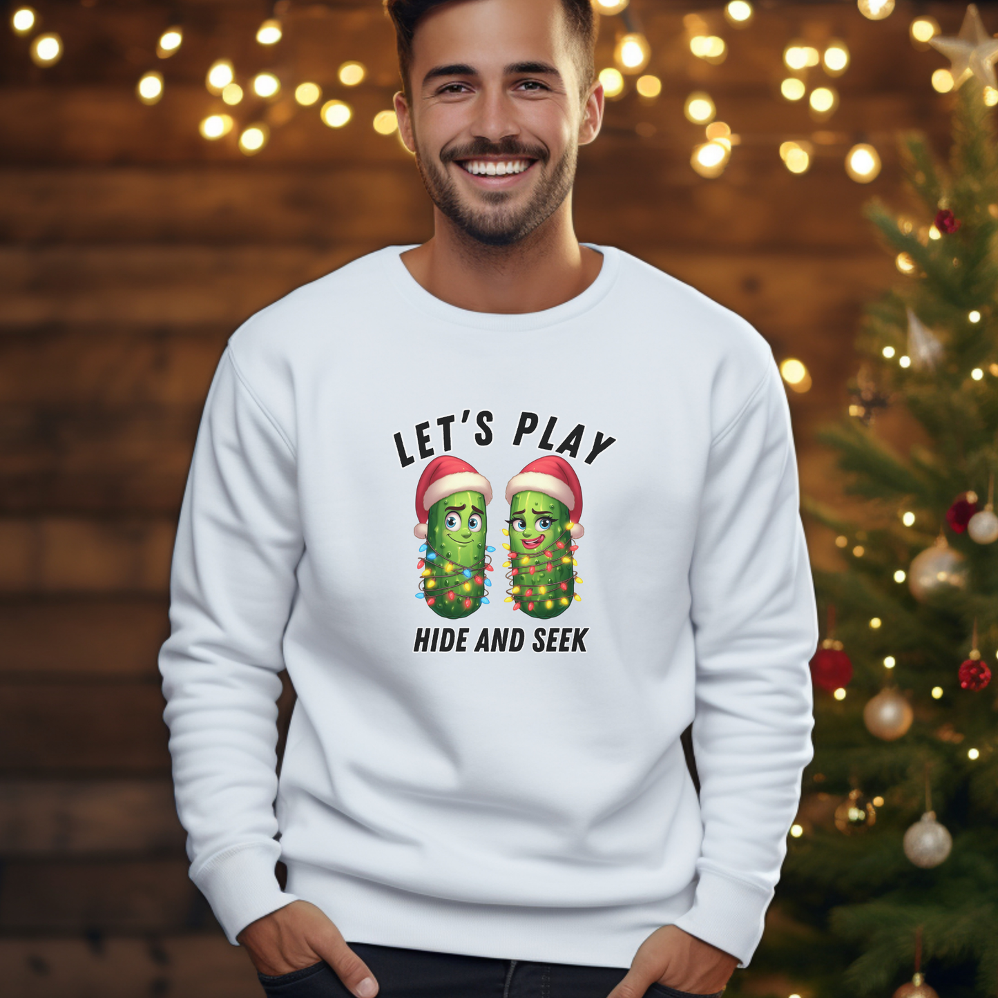 Man wearing a white sweatshirt with Christmas pickle design in front of a decorated Christmas tree.
