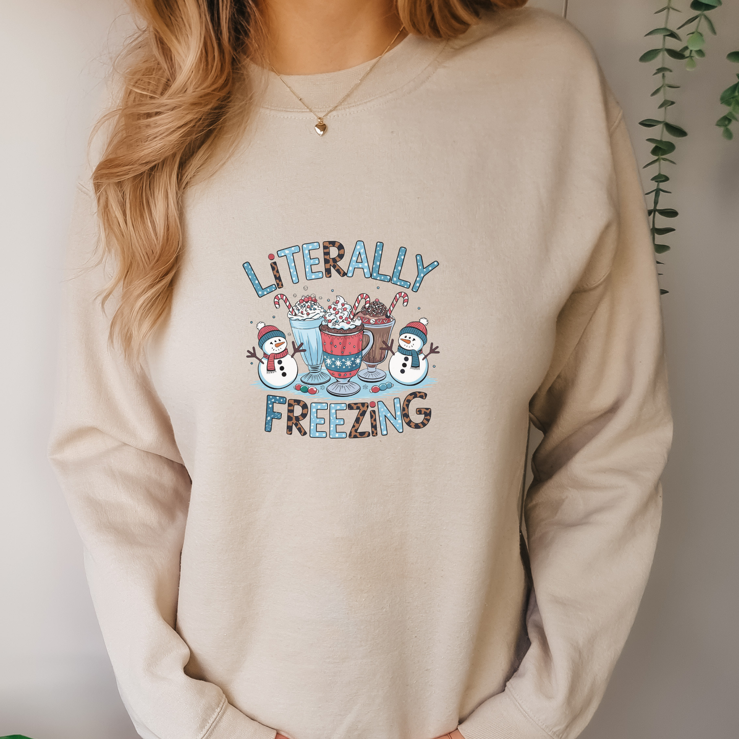 Beige sweatshirt with literally freezing text and snowmen and cocoa graphics