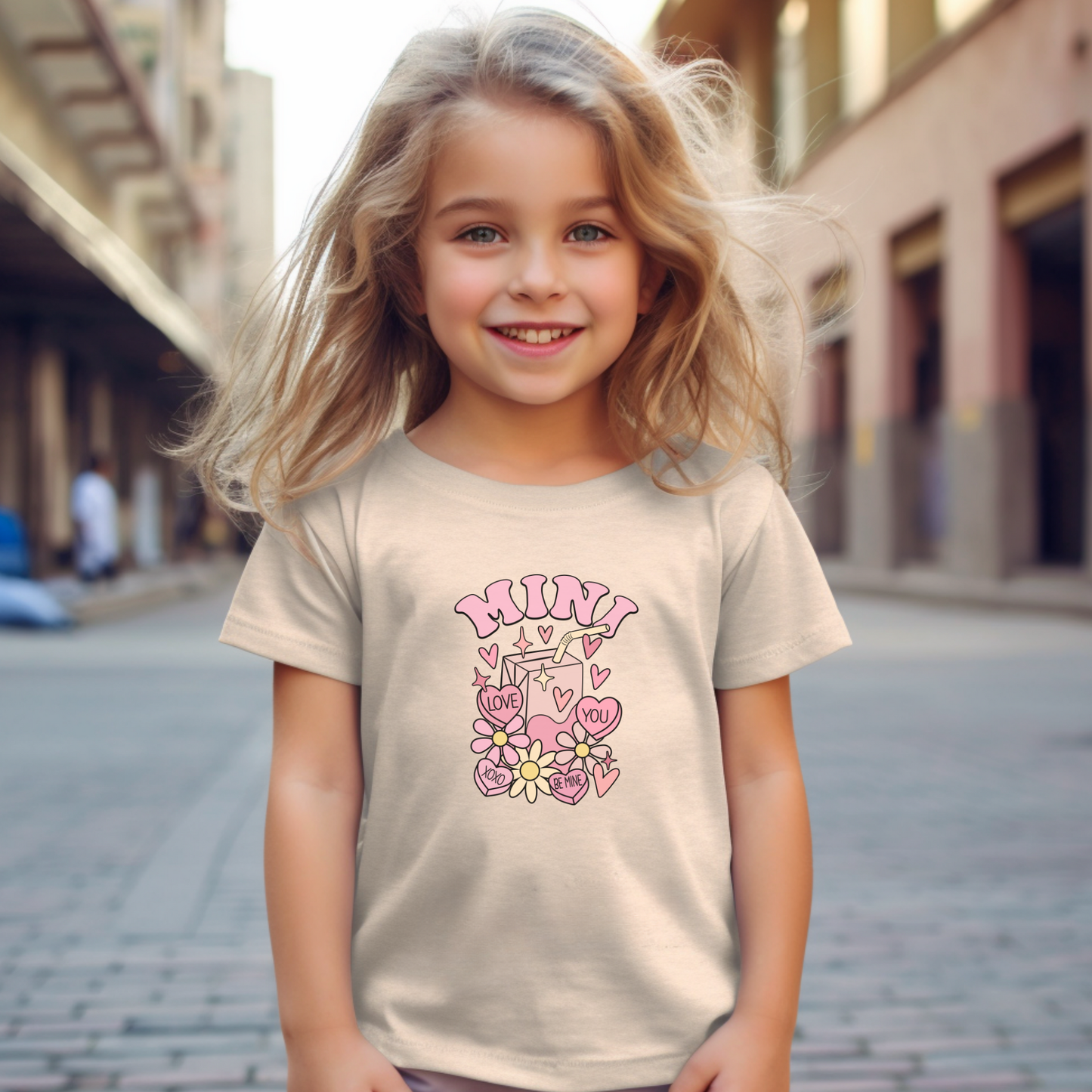 Young girl wearing a beige t-shirt with pink graphics and text, mini Valentine's tee