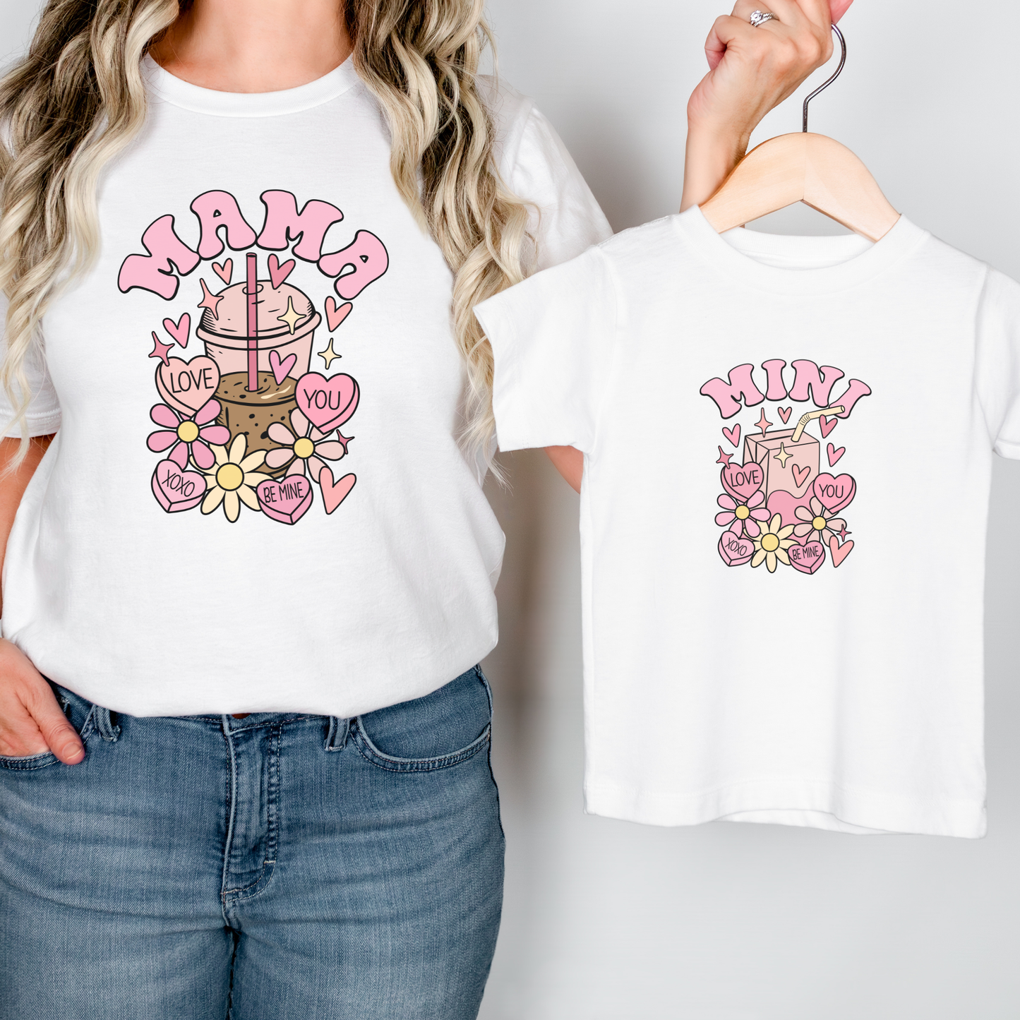 Two white t-shirts with colorful graphics of a coffee cup and text, one worn by a person and the other on a hanger. mama mini valentines shirts