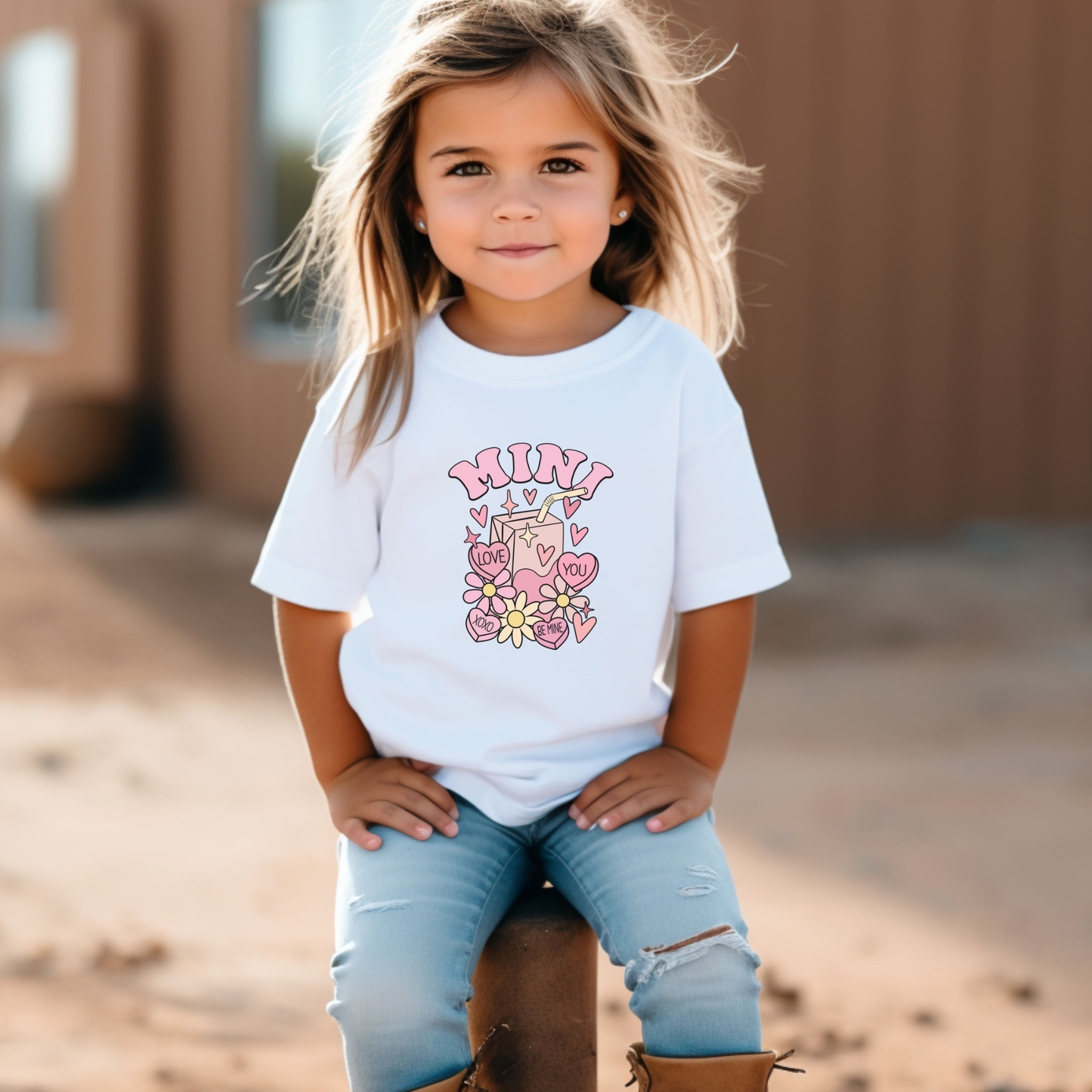 Young girl wearing a white t-shirt with pink graphics and text, standing outdoors. mama mini matching tee, valentintes day