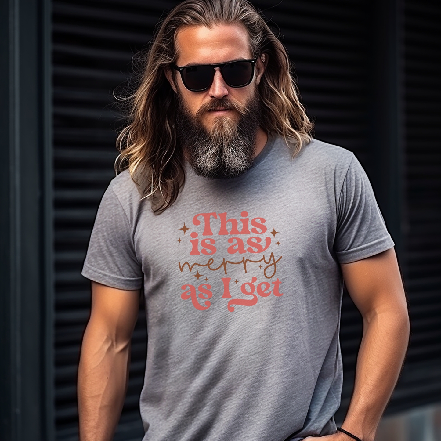 Man wearing a gray t-shirt with a humorous quote, standing against a dark background. this is as merry as i get 