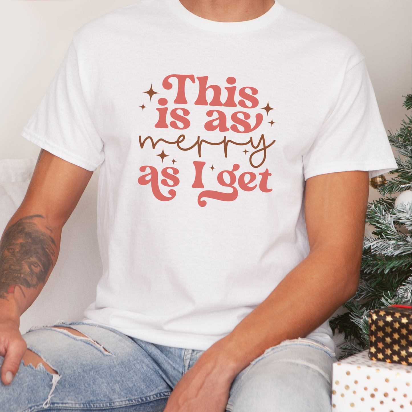 Person wearing a white t-shirt with red text in front of a Christmas tree.