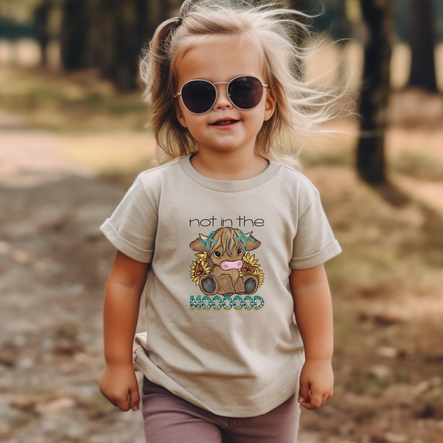 Child wearing sunglasses and a t-shirt with a graphic design outdoors, not in the mood, baby highland cow