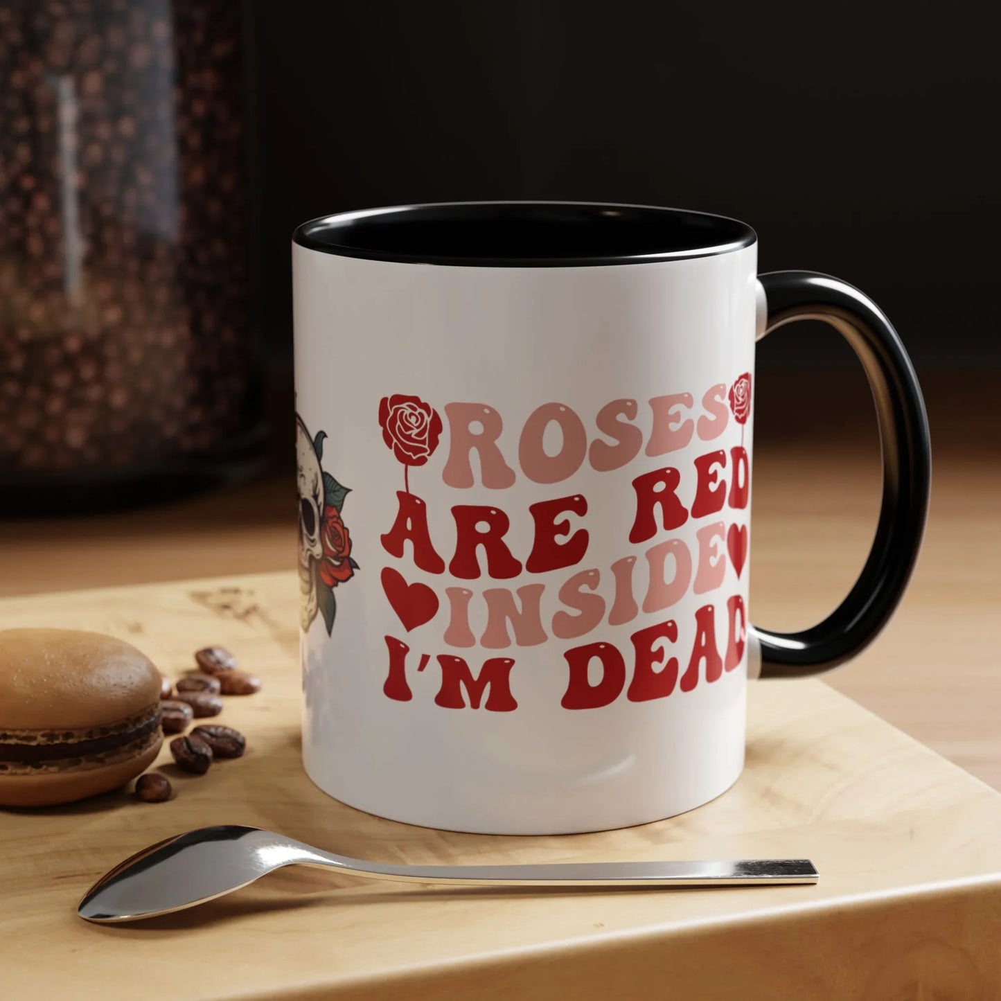 White mug with red text and black handle on a wooden surface with coffee beans and a spoon. roses are red, inside I'm dead, floral skull design, 11oz