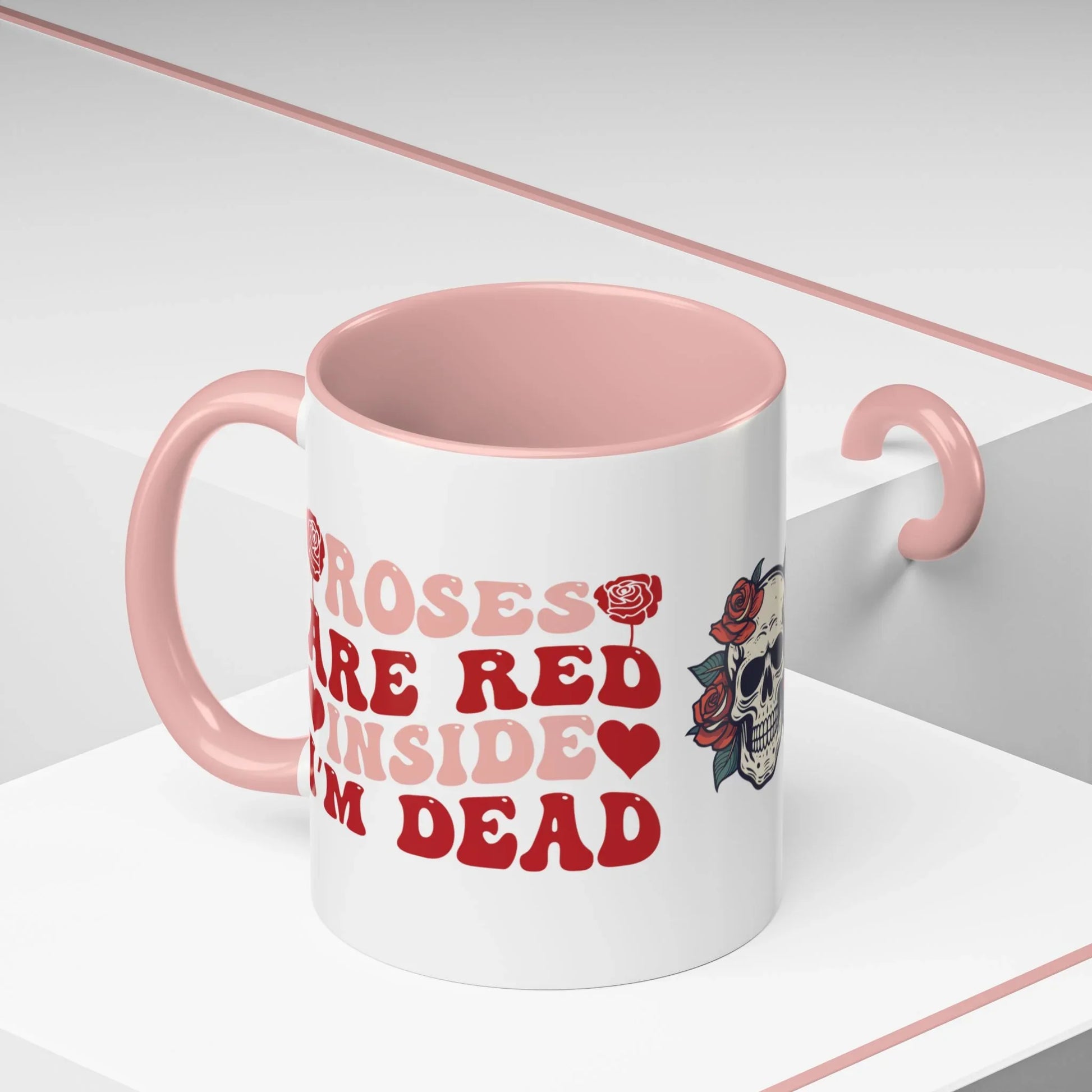 White mug with pink interior and handle, featuring red text and a floral skull design on a white background. roses are red, inside I'm dead, 11oz