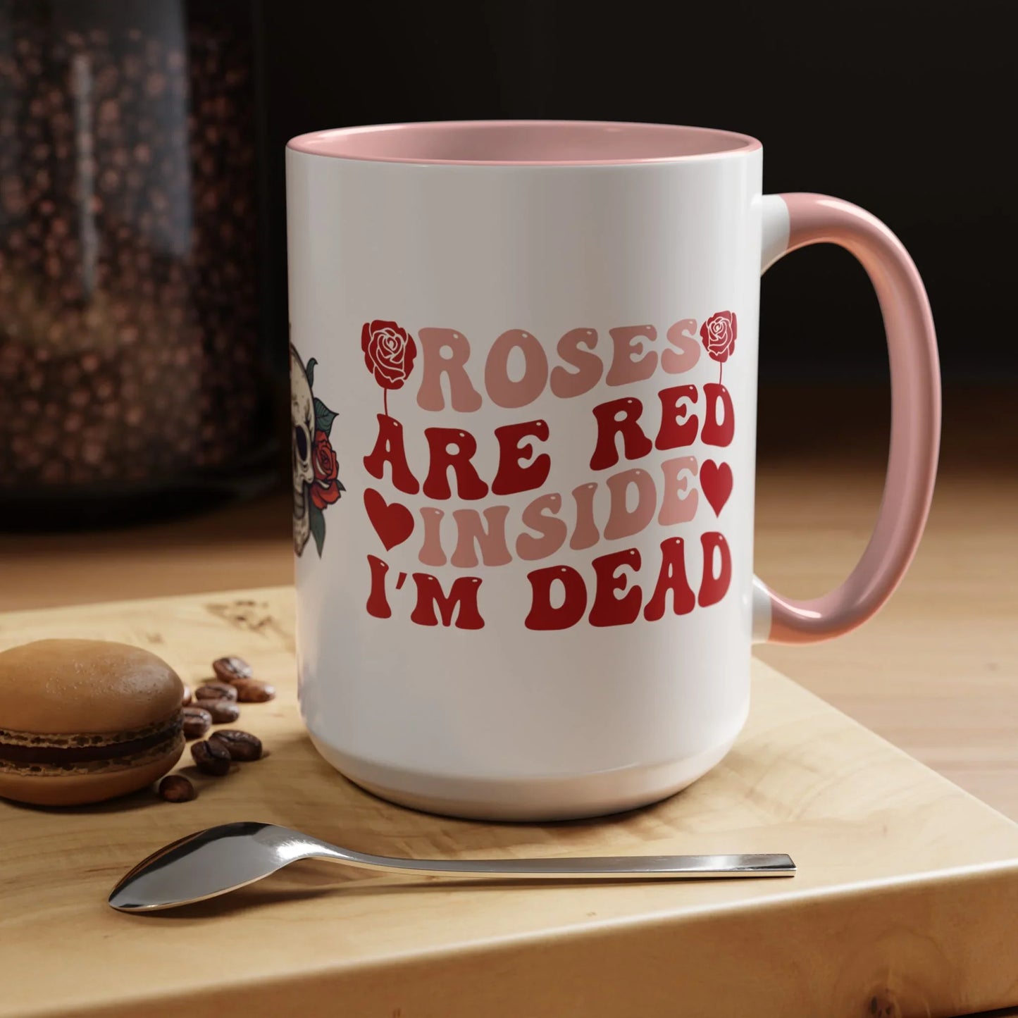 White mug with red text and pink handle on a wooden surface with coffee beans and a spoon. roses are red, inside I'm dead, floral skull design, 15oz