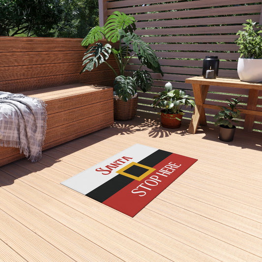 Decorative mat with 'Santa Stop Here' text on a wooden deck with plants and furniture.