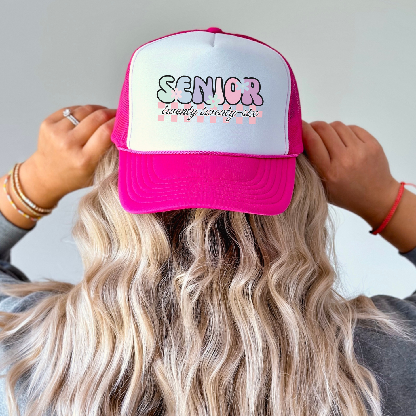 Person wearing a pink and white cap with 'Senior twenty twenty-six' text.