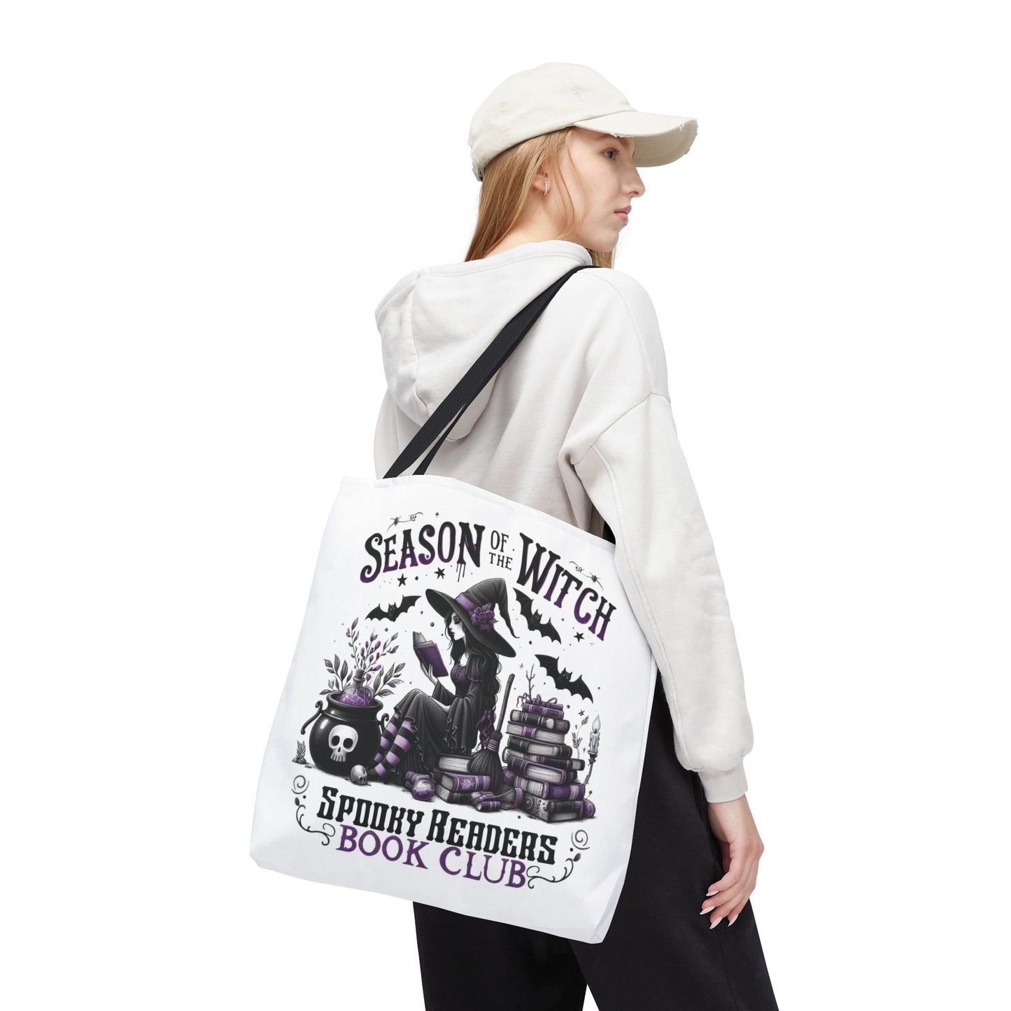 Person wearing a white hoodie and cap, carrying a tote bag with Halloween-themed design. season of the witch book club